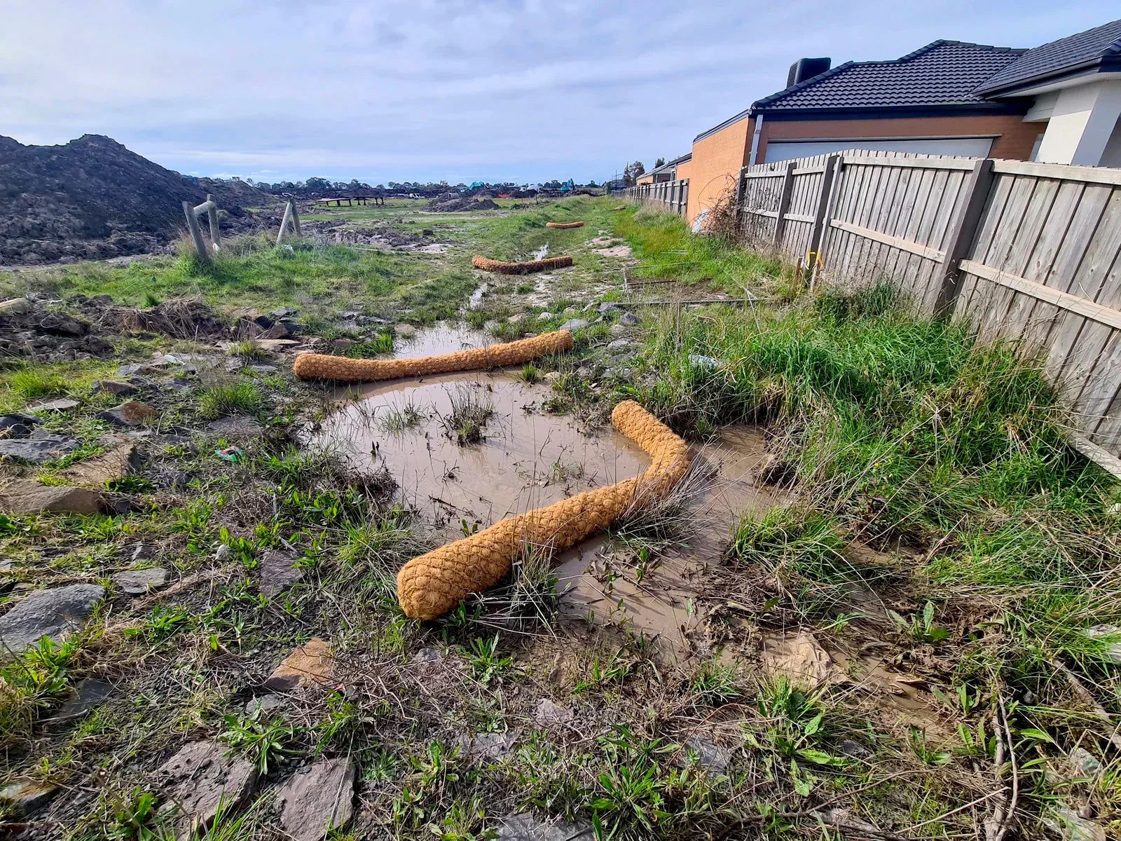 Coir logs placed to slow water flow and prevent erosion in a muddy area after heavy rain