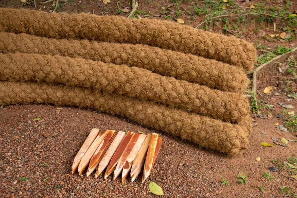 Several brown coir logs made from coconut husk fiber stacked on the ground with wooden stakes nearby