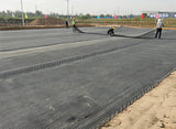Construction workers laying out a large HDPE uniaxial geogrid on a flat surface.