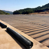 Roll of HDPE uniaxial geogrid on a concrete surface with a forested area in the background