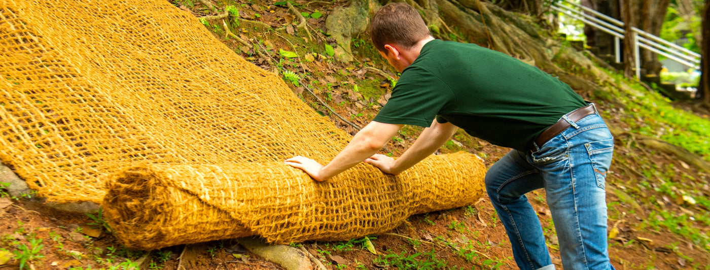 Person unrolling coir mesh on a slope