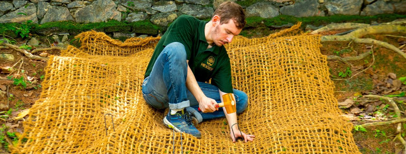 Person hammering a retaining pin into a coir mesh outdoors