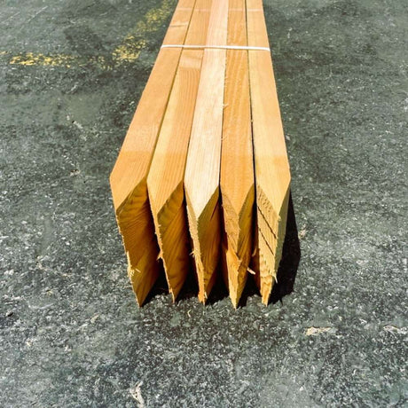 Bundle of five pointed wooden pegs laid out on a concrete surface for gardening or fencing use