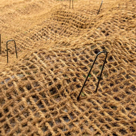 HEIGER coir mesh laid over soil with metal pins securing natural fiber erosion control fabric