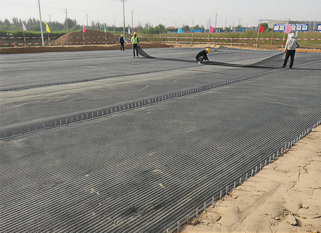 Workers installing HDPE Uniaxial Geogrid over ground for soil stabilization and infrastructure support