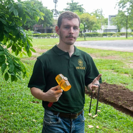 HEIGER worker holding weed mat pins and a rubber mallet for garden installation