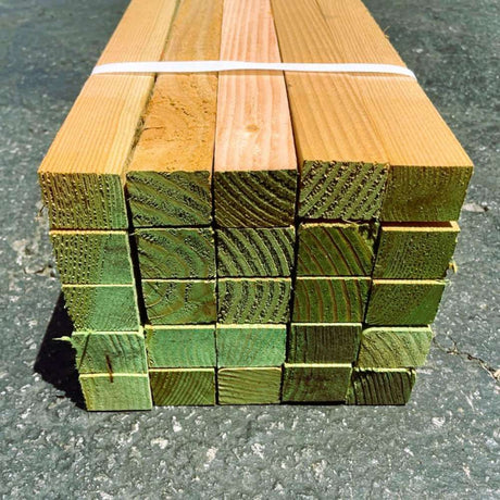 Stack of green-treated wooden pegs bundled together and placed on asphalt surface