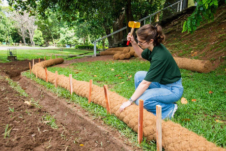 HEIGER coir logs being installed along garden edge for erosion control by a woman with a rubber mallet